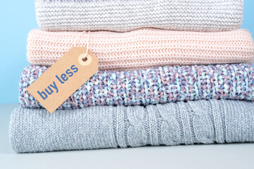 Stack of winter sweaters with the buy less tag. Conscious consumption. Environmental friendliness and sustainable fashion