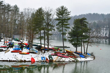 Fototapeta premium Colorful canoes, kayaks and rowboats, laying in the snow by a lake in the winter