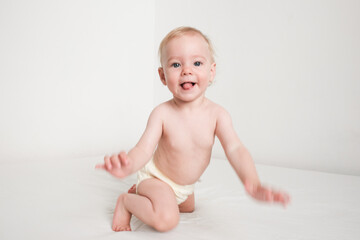 Happy baby in panties is playing on white bed in white room