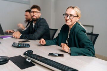 Portrait of cheerful businesswoman in suit laughing at funny joke with young coworkers in office....