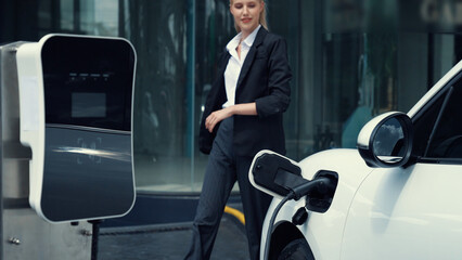Progressive businesswoman unplug charger plug from charging station to his electric car before...
