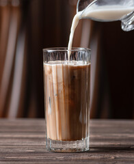 Milk is poured into a glass with coffee and ice