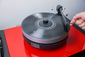 View of person's hands as they high-fidelity vinyl record player and lower tonearm onto vinyl to...