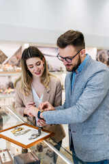 Fototapeta premium Elegant middle age businessman choosing and buying his new expensive watch. Beautiful young female seller helps him to make good decision. Fashion style and elegance concept.