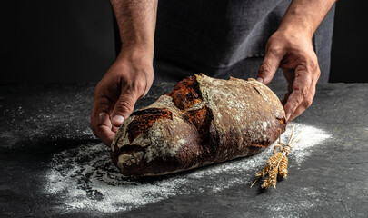 Homemade sourdough bread in hand on a dark background. banner, menu, recipe place for text, top view