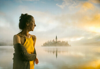 Woman in yellow dress watching a sunrise among the fog on the shores of Lake Bled, Slovenia