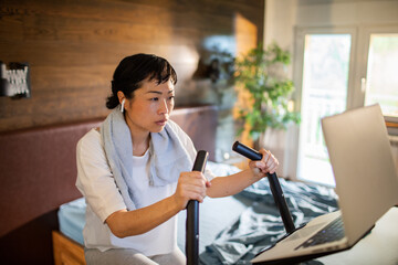 Young Asian woman using the laptop while on a exercise bike at home
