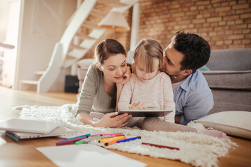 Curious little girl using the tablet with her parents on the living room floor
