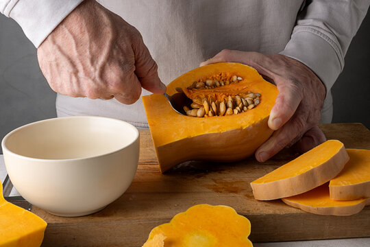 Caucasian man is cleaning a ripe pumpkin from seeds in the kitchen.