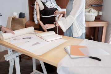 Fashion seamstress woman use tape measure to measuring fashion clothes on mannequin and taking note.