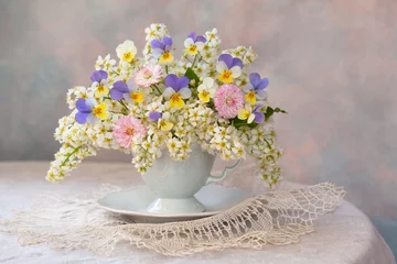 Fotobehang Viooltje A bouquet of spring flowers: bird cherry, daisies, pansies in a cup on the table, beautiful composition, still life, holiday card.  © tachinskamarina