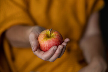 Ripe apple in a woman's hand on a yellow background.