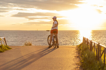Girl on a bicycle at sunset near the sea.