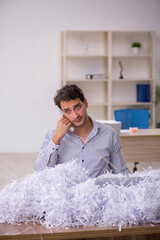 Young male employee and a lot of cut papers in the office