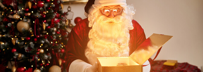 Surprised Santa Claus with glowing gift near christmas tree. New year and Merry Christmas concept