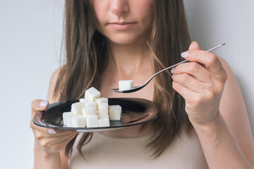 a young caucasian brunette woman in a beige underwear holds a black plate with refined sugar in front of her, and in her other hand holds a spoon with sugar, wants to eat it