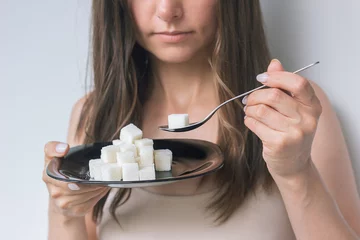 Foto op Canvas a young caucasian brunette woman in a beige underwear holds a black plate with refined sugar in front of her, and in her other hand holds a spoon with sugar, wants to eat it © Ольга Шефер
