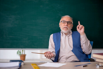 Old male teacher in front of green board