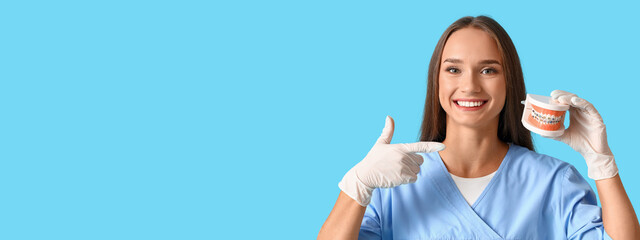 Smiling female dentist holding plastic jaw model on light blue background with space for text
