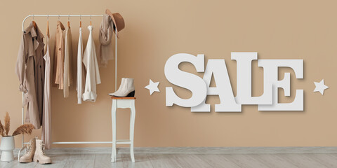 Rack with stylish clothes, shoes and word SALE against beige wall