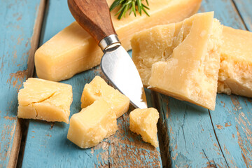 Pieces of tasty Parmesan cheese on blue wooden background, closeup