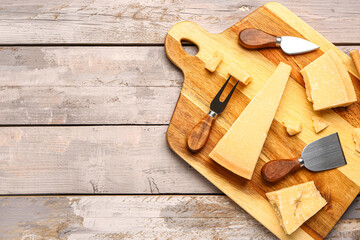 Board with pieces of tasty Parmesan cheese on light wooden background, closeup
