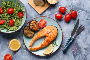 Plate with tasty grilled salmon steak and vegetables on blue background