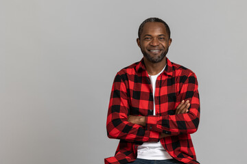Smiling black bearded man wearing red checkered shirt keeps hands folded