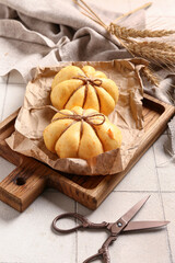 Wooden board with pumpkin shaped buns on white tile background