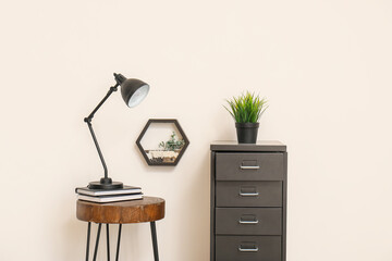 Desk lamp on small table and file cabinet with houseplant near white wall