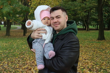 dad holds a little girl in his arms in the park in autumn