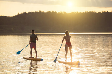 Man and woman sup board surfers at sunset.