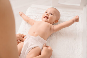 Mother putting diaper on her cute little baby at changing table