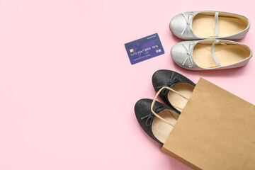 Shopping bag with stylish child's shoes and credit card on pink background