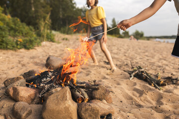 Children's hand with marshmallow on stick roasted on fire summer on beach