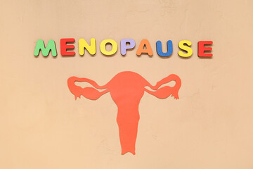 Word MENOPAUSE with paper uterus on beige background