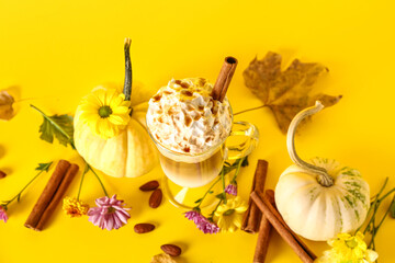 Glass cup of tasty pumpkin latte with cinnamon and almond on yellow background