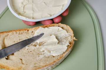 Man cuts a piece of fresh bread with a knife and makes a delicious cheese sandwich in the kitchen
