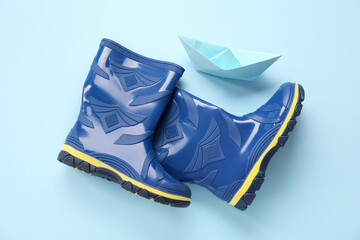 Blue gumboots and paper ship on color background