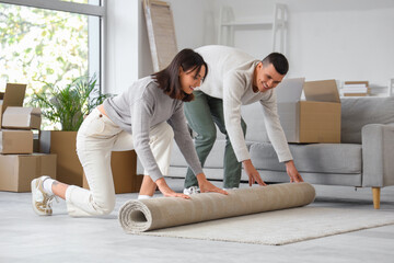 Happy young couple rolling carpet in room on moving day