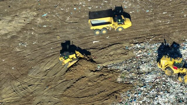 Solid waste disposal facility. Landfill dump site for garbage managment. Bulldozer tractors burying large amount of trash under the ground. Harmful impact of modern consumerism on environment