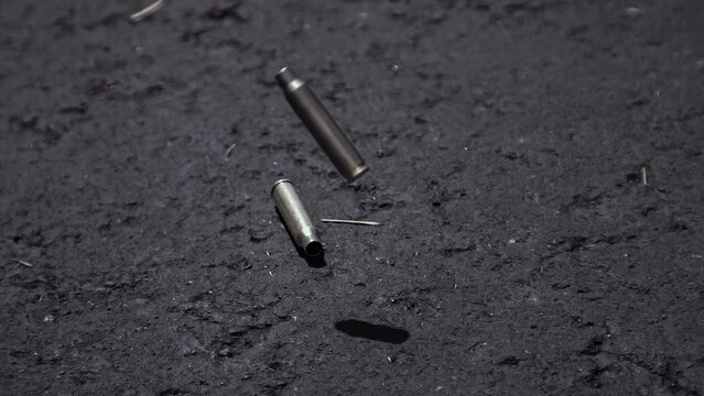 Empty bullet shell casings falling on asphalt ground in 1000fps slow motion