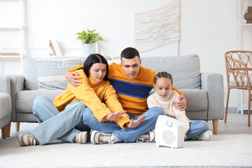 Frozen family warming near electric fan heater at home