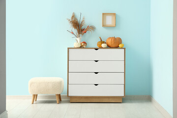 Chest of drawers with pumpkins and pampas grass near blue wall