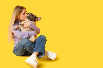 Obraz na płótnie Canvas Beautiful young woman kissing her cute pug dog on yellow background