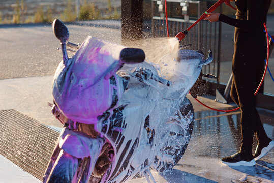 Beautiful girl washes a motorcycle at self service car wash with high pressure water.
