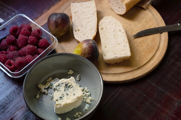 Baguette with blue cheese, figs and raspberries on wooden cutting board