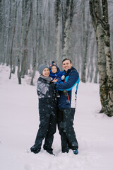 Fototapeta na wymiar Smiling parents with a small child in their arms stand under snowfall in the forest