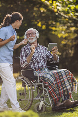 Senior man in wheelchair with nurse listening music in park