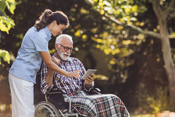 Senior man in wheelchair and nurse looking at tablet